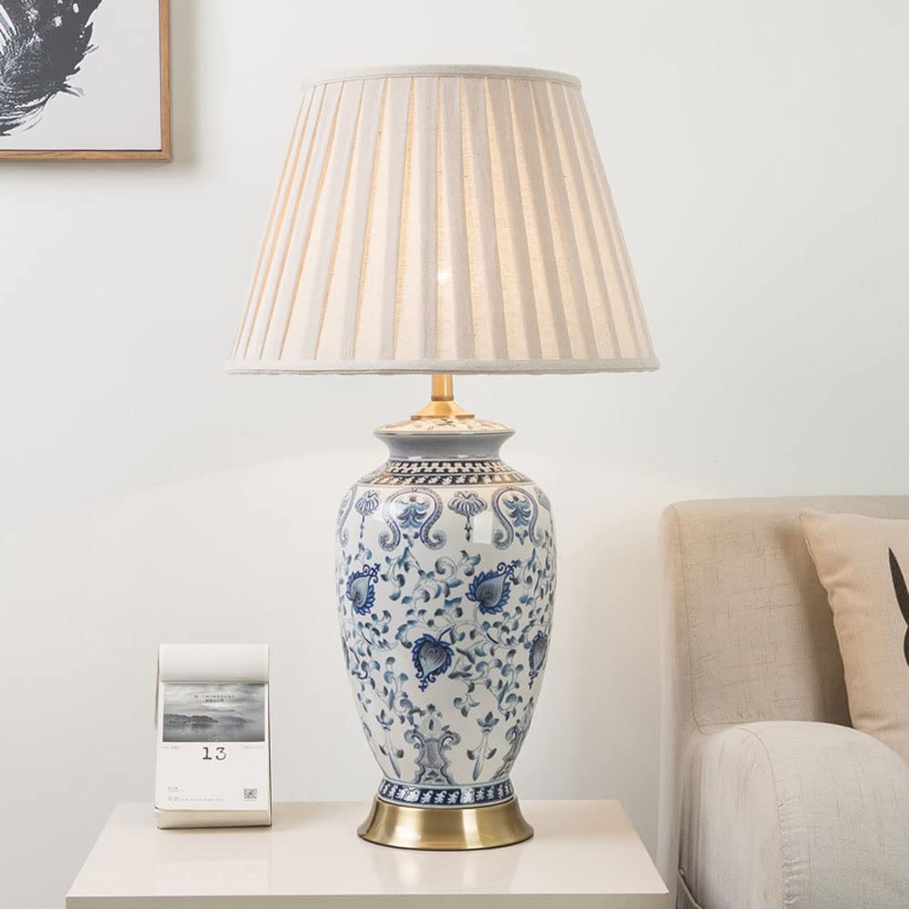 GLOW KANAGAWA WAVE TABLE LAMP with blue floral patterns on a white surface, with a couch and framed picture in the background.